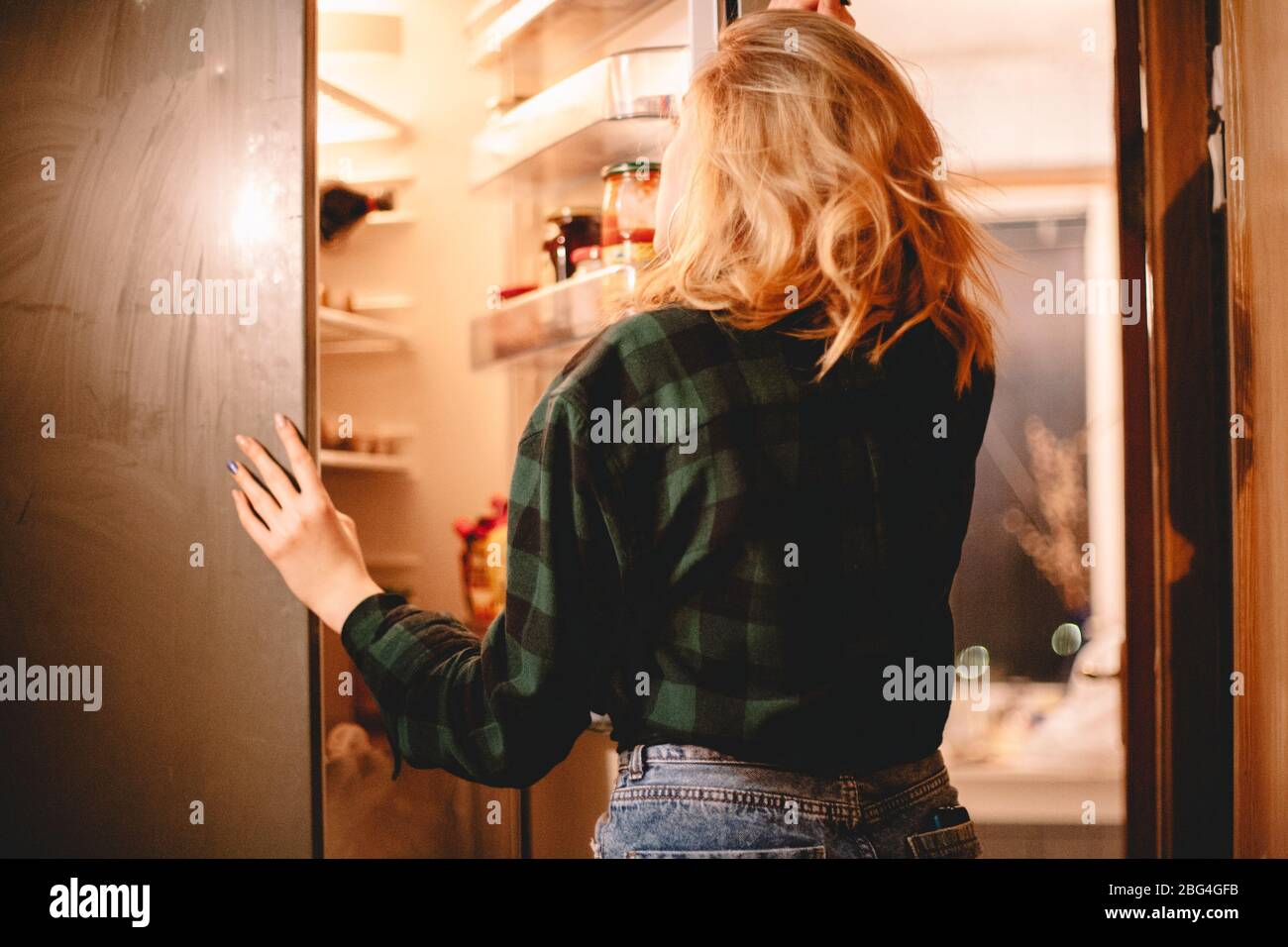 Junge hungrige Frau, die zu Hause im offenen Kühlschrank steht Stockfoto