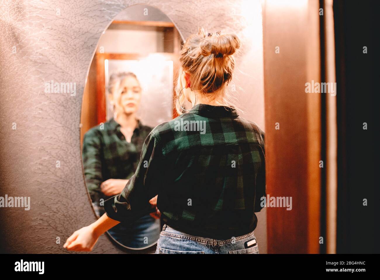 Junge selbstbewusste Frau, die sich im Spiegel ansieht, während sie zu Hause im Flur steht und sich vor dem Ausgehen fertig macht Stockfoto