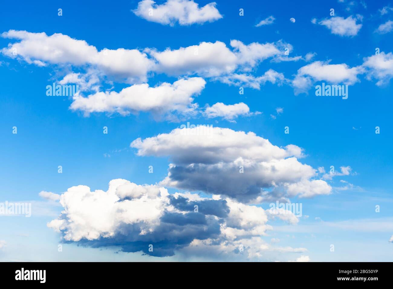 Wenige niedrige dunkle Regenwolken und viele kleine weiße Wolken am blauen Himmel am Märztag Stockfoto