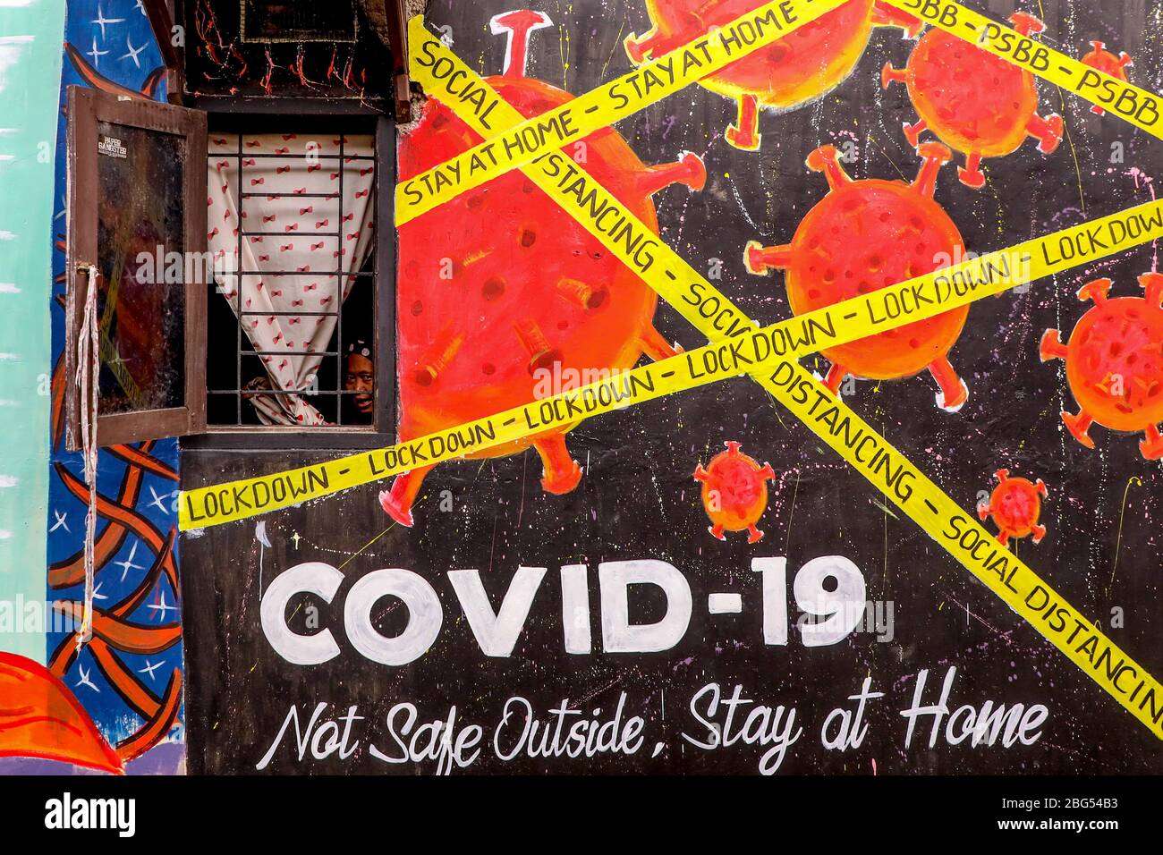 Eine Frau zieht durch ein Fenster ihres Hauses, das während einer Sperrung  mit einem Graffiti über das Coronavirus-Bewusstsein gemalt wurde.  Indonesische Künstler zeichneten Wandmalereien an den Wänden der Häuser, um  die Bevölkerung