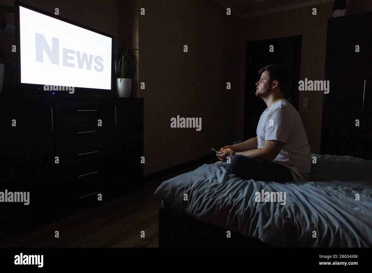 Junger Erwachsener Mann auf Bett sitzen und Fernsehen Stockfoto