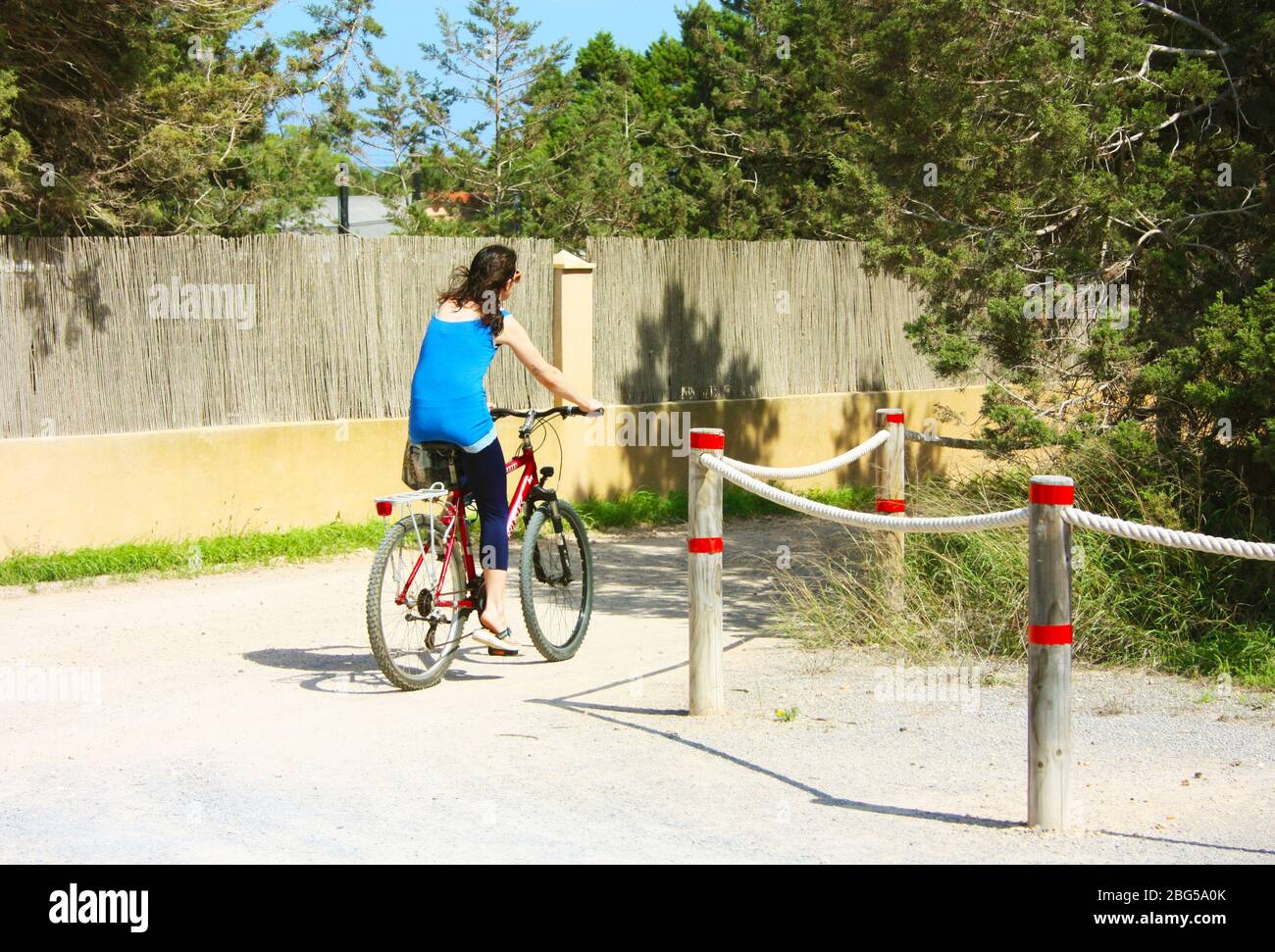 kaukasisches Mädchen fährt an einem sonnigen Tag auf Ibiza ein Fahrrad durch die unbefestigten Straßen im trockenen balearischen Klima Stockfoto