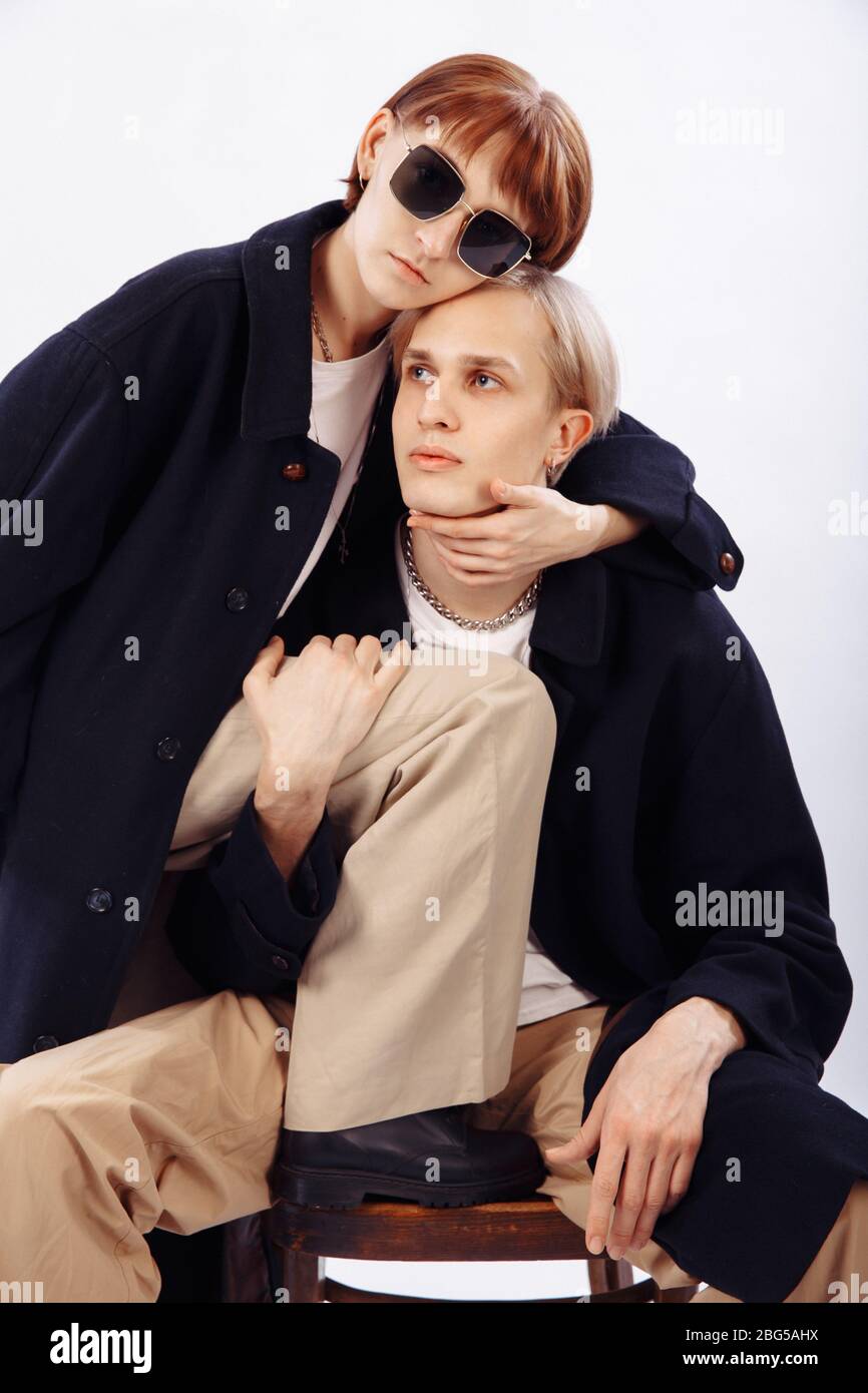Stil 90. Ein Mädchen und ein Kerl stilvoll gekleidet. Der blonde Mann sitzt auf einem Stuhl und schaut weg. Das Mädchen umarmt den Kerl. Stockfoto