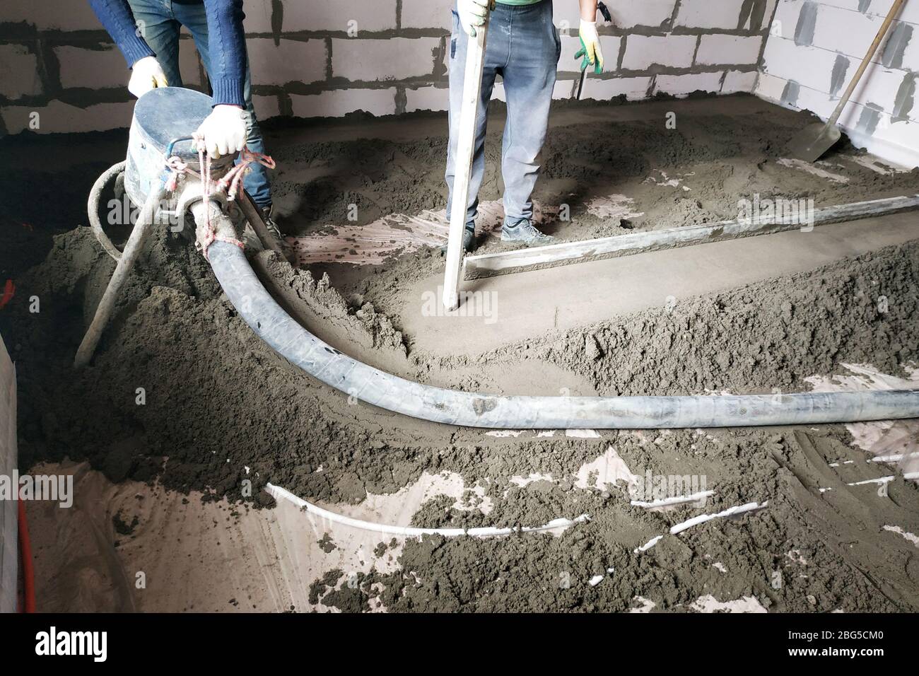 Der Arbeiter führt einen Sand-Zement-Bodentrich über der Fußbodenheizung durch.2020 Stockfoto