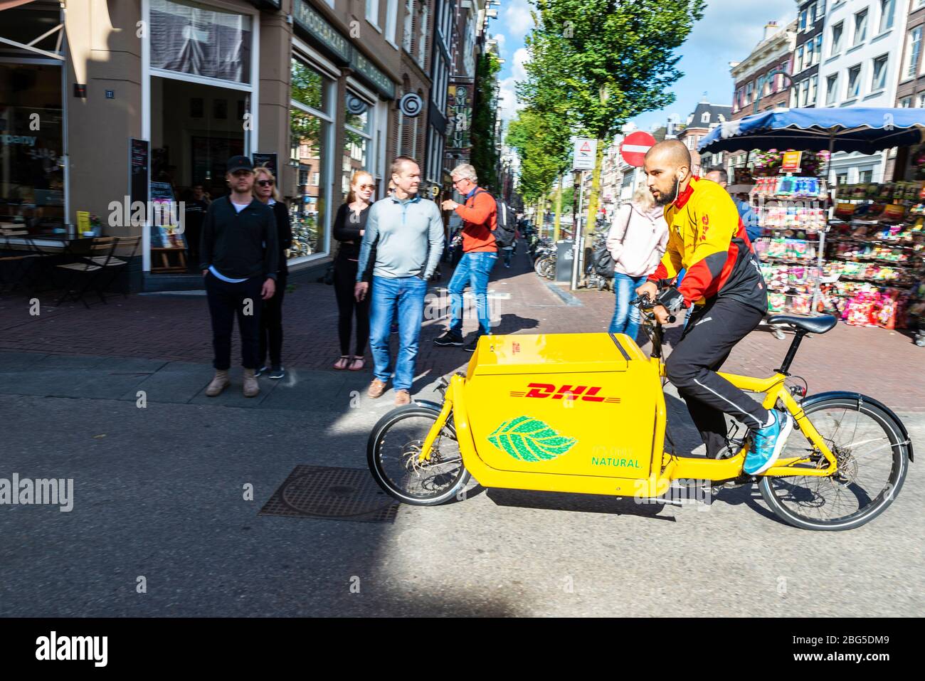 Amsterdam, Niederlande - 7. September 2018: Junger Mann auf dem Lieferfahrrad DHL zirkulierend und Menschen zu Fuß in einem alten historischen Zentrum von Amsterdam, N Stockfoto