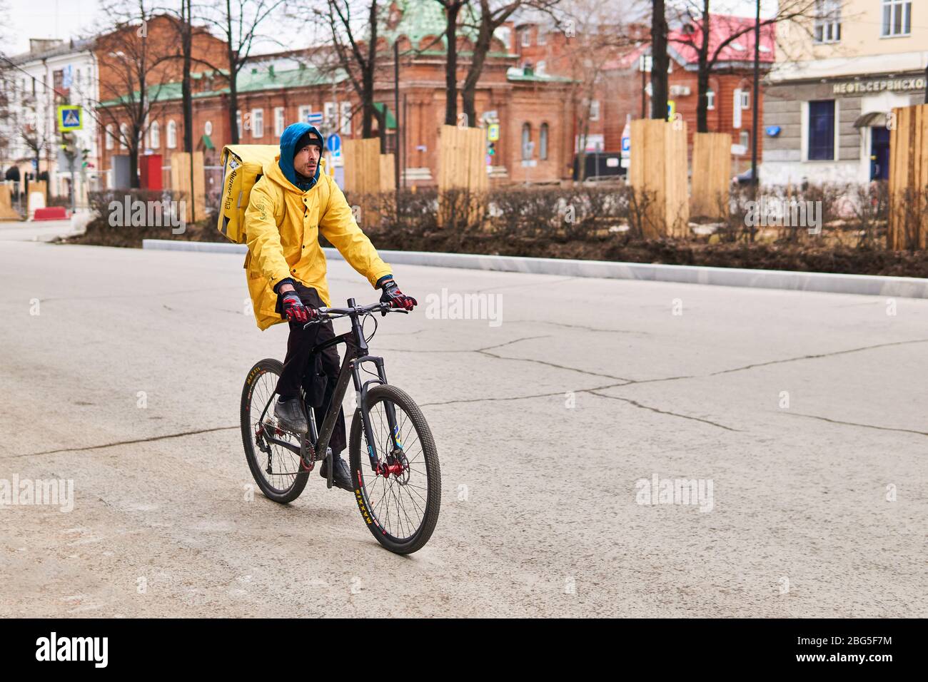 Perm, Russland - 19. April 2020: Kurier-Online-Lebensmittelzustelldienst fährt ein Fahrrad auf einer leeren Straße während einer Coronavirus-Pandemie Stockfoto