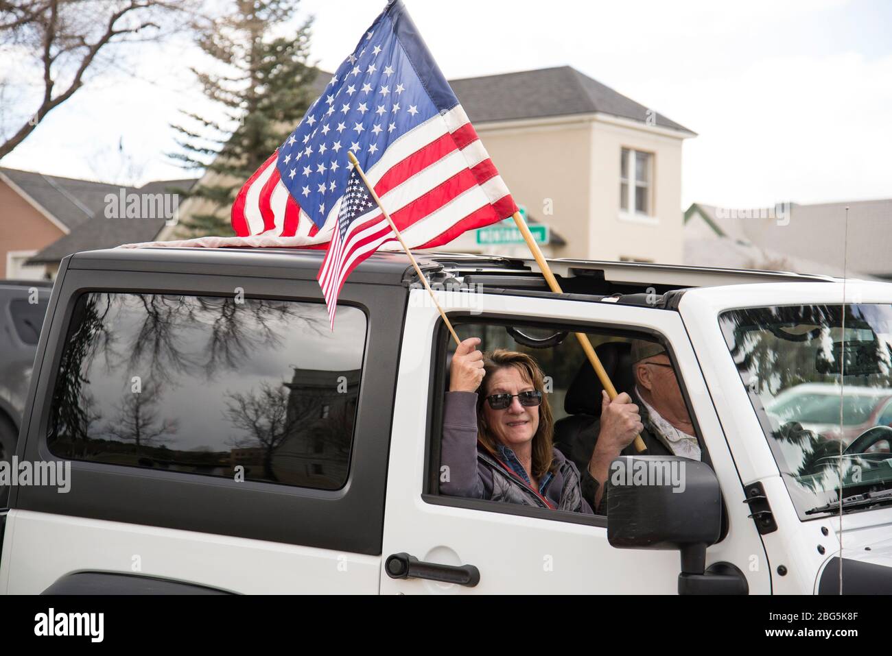 Helena, Montana - 19. April 2020: Mann und Frau halten amerikanische Fahnen in einem weißen Jeep bei einer Freiheitskundgebung um den Capitol Square gegen den Shutdo der Regierung Stockfoto