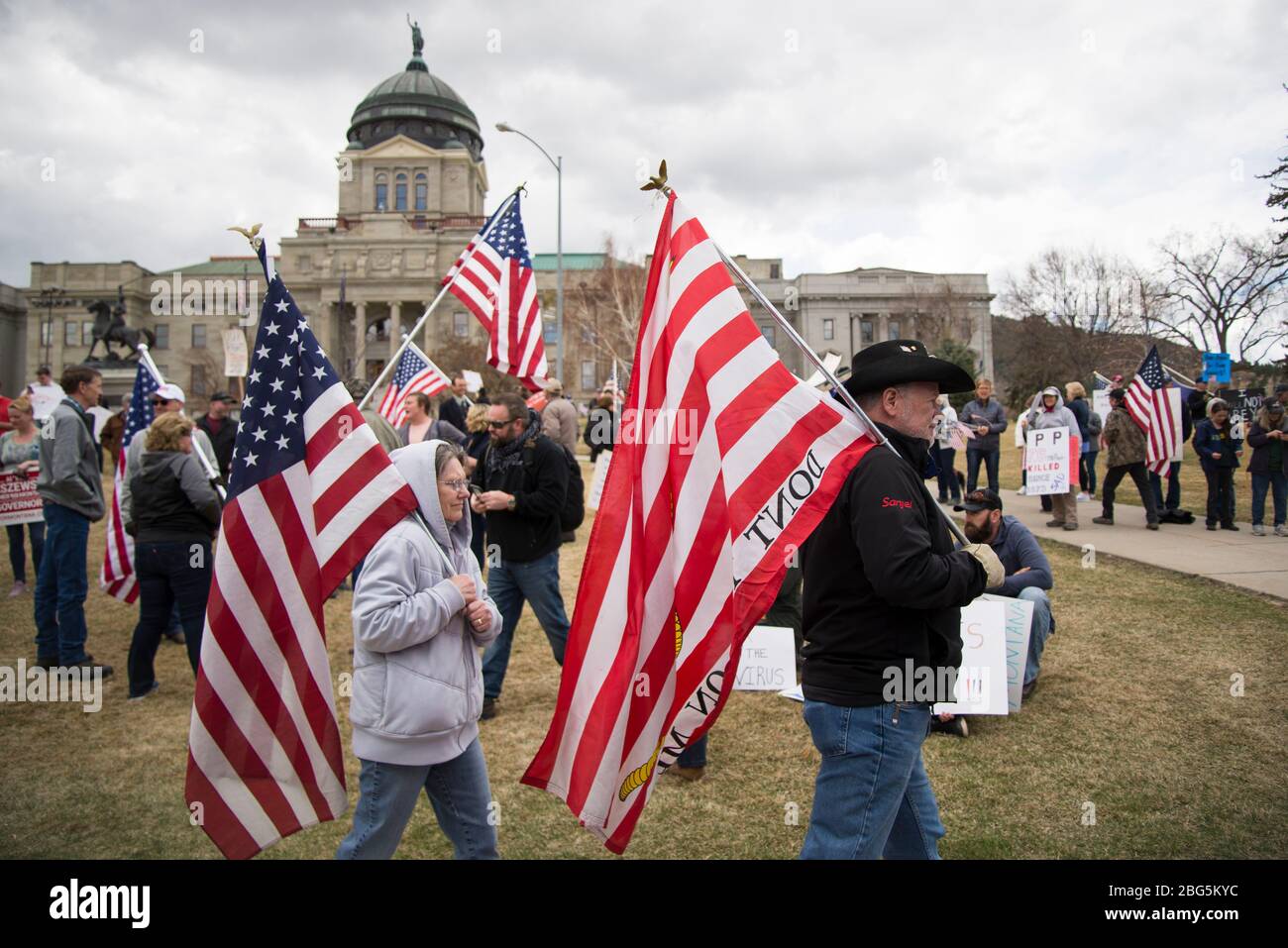 Helena, Montana - 19. April 2020: Protestierende, ein Mann und eine Frau, die amerikanische Flaggen halten, marschieren bei einem Protest gegen die Schließung der Regierung. Stockfoto
