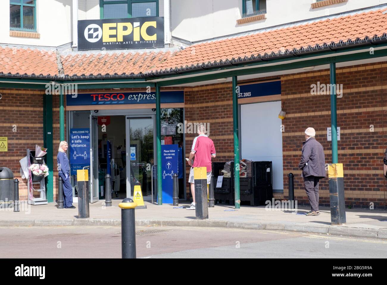 Käufer, die während der Sperrung des Covid-19 bei einem Tesco Express anstehen, halten sich an die Regeln für soziale Distanzierung. Stockfoto
