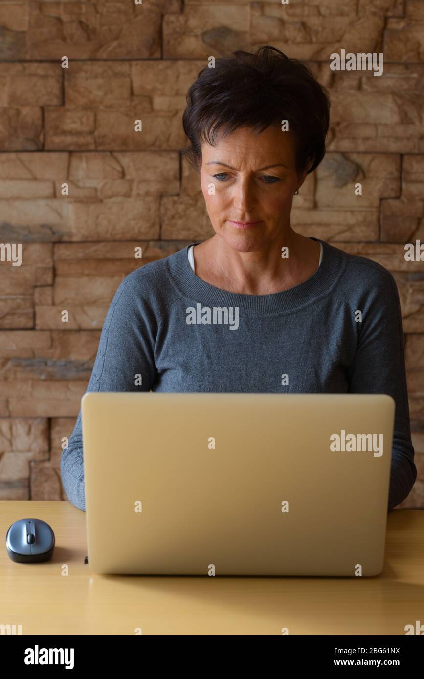 Reifen schöne Frau mit Laptop auf Holztisch gegen Ziegelwand Stockfoto
