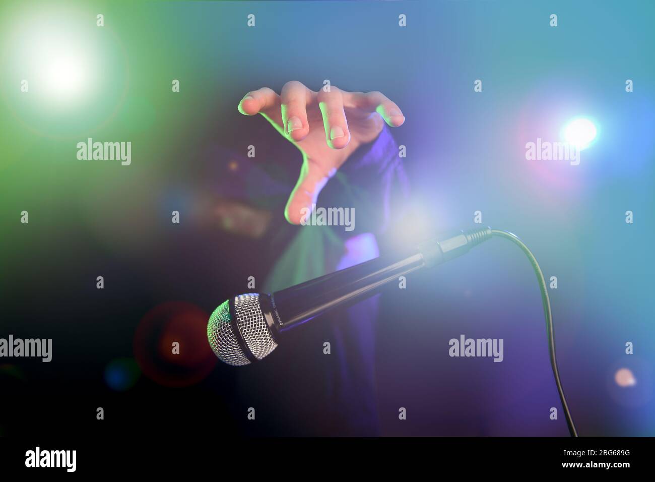 Bild des Mikrofonkonzepts ablegen. Aufgenommen mit Bühnenbeleuchtung, mehrfarbigem Effekt und coolem Kerl mit Hoodie. Stockfoto