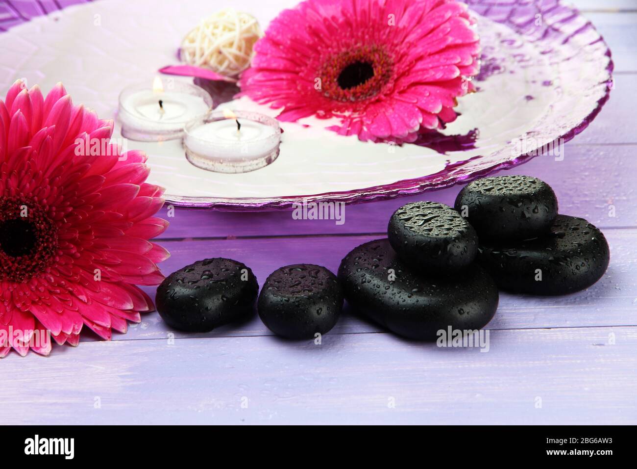 Spa-Steine, wunderschöne Gerbera-Blumen und Kerzen auf dem Wasser Stockfoto