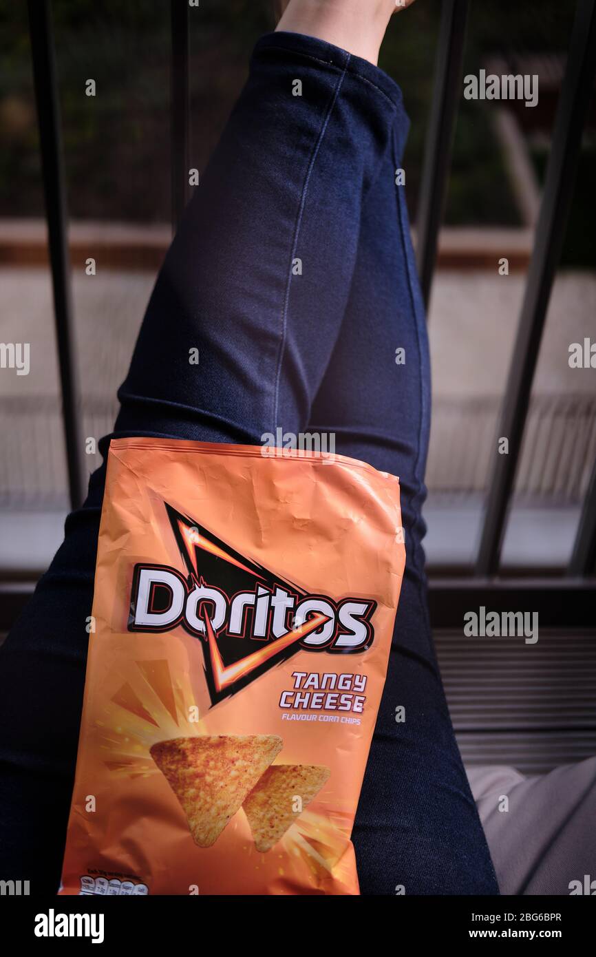 Ein orangenes Päckchen würziger Käse doritos, der auf dem Schoß einer Frau in blauer Jeans liegt Stockfoto