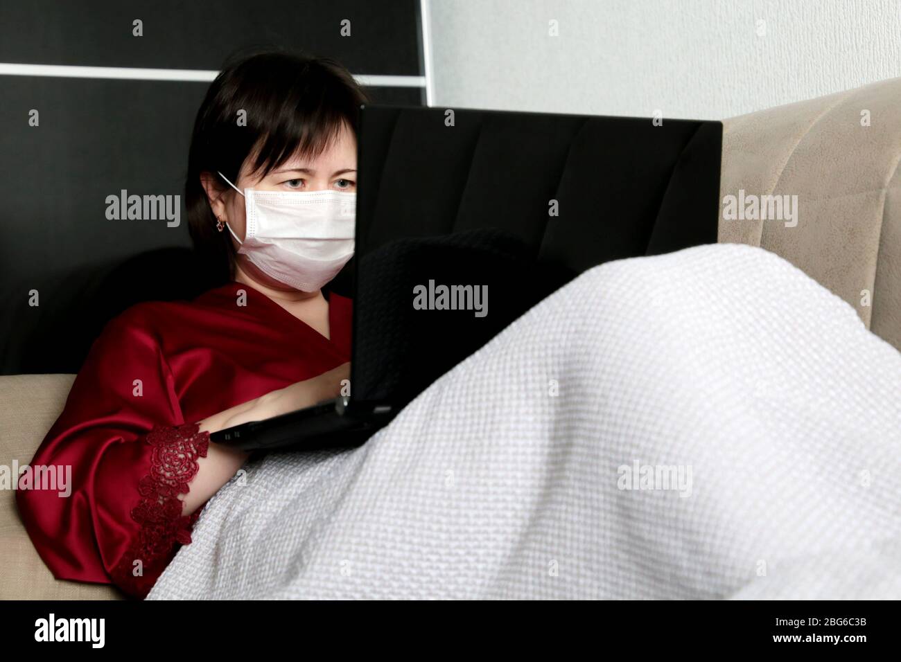 Frau in medizinischer Gesichtsmaske sitzt auf einem Sofa mit einem Laptop. Konzept der Remote-Arbeit während einer COVID-19 Coronavirus-Epidemie, Home Quarantäne Stockfoto