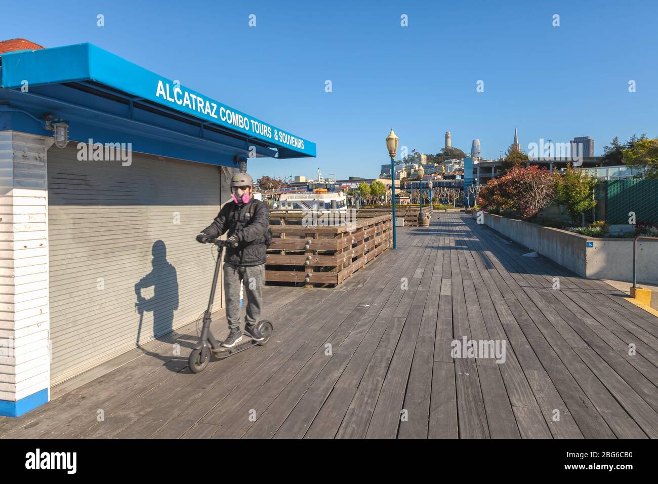 Mann mit Maske und Schutzkleidung fährt auf dem Roller am Pier 39 während der Stadtsperrung wegen COVID-19 Pandemie, San Francisco, Kalifornien, USA. Stockfoto