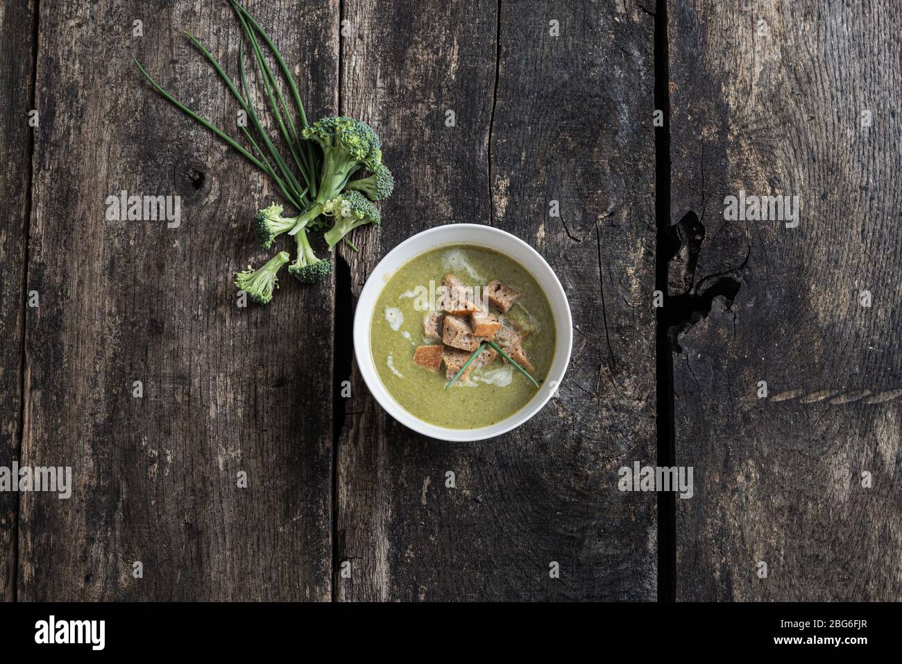 Draufsicht der köstlichen cremigen Brokkoli-Suppe mit hausgemachten Croutons Brot und Hafercreme. Auf rustikalem Holzschreibtisch mit Brokkoli und Schnittlauch an der Seite. Stockfoto