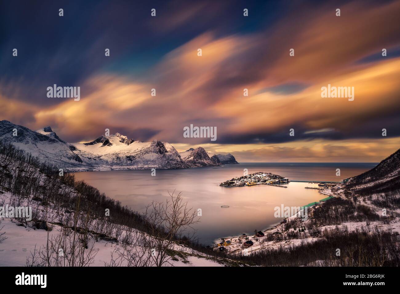 Das warme Licht bei Sonnenuntergang, das auf Wolken, Streifen über den schneebedeckten Bergen und schönen Fjord, mit einem Fischerdorf auf einer Insel. Stockfoto