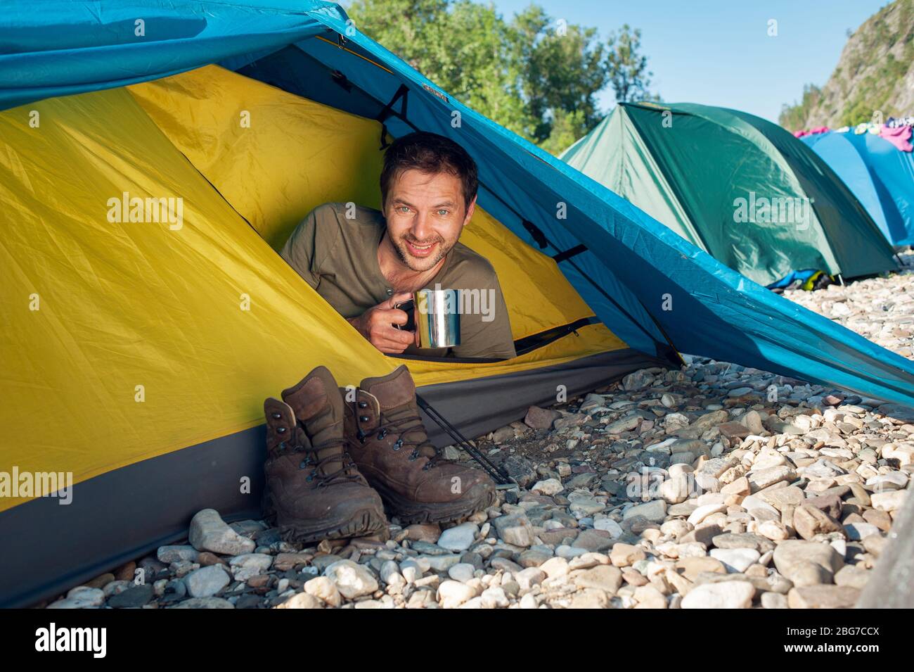 Männlicher Tourist trifft guten sonnigen Morgen, sitzen im touristischen Zelt mit einer Tasse heißen Tee. Active Vacation Concept-Bild. Stockfoto