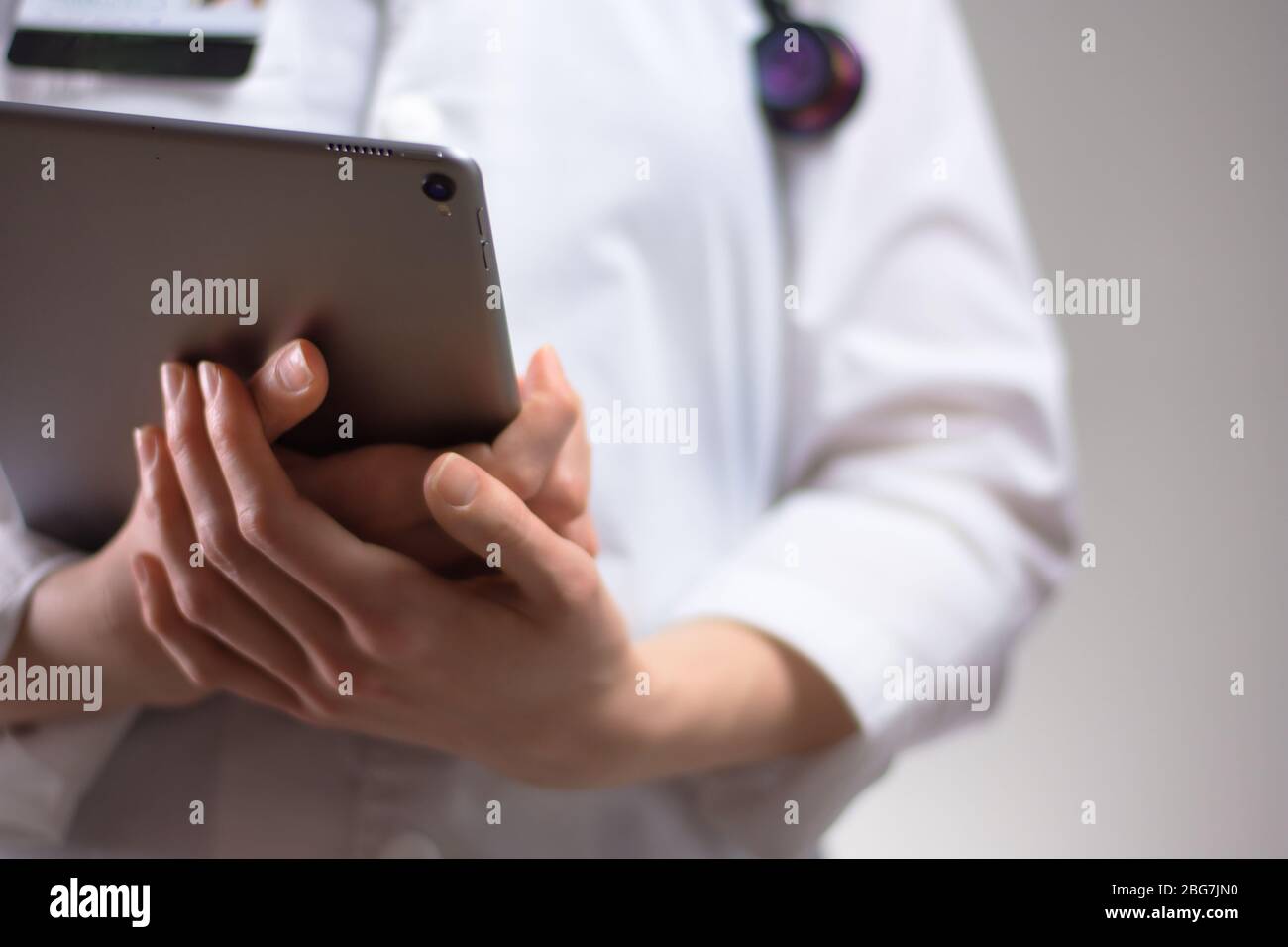 Tablet in den Händen von Gesundheitsexperten aus nächster Nähe. Weißes Fell, Stethoskop und Abzeichen im Hintergrund sichtbar. Hände eines Pflegefachpersonals oder PA U Stockfoto