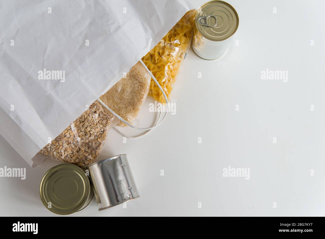 Verschiedene Dosengerichte, Pasta, Reis und rohe Getreidekörner auf einem Tisch in Papiertüte mit Kopierplatz Stockfoto