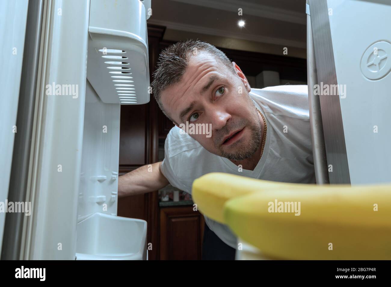 Mann geht während der Selbstisolierung in einen leeren Kühlschrank. Schockierter Mann, der zu Hause in einen leeren Kühlschrank schaut. COVID-19. Coronavirus-Konsequenz Stockfoto