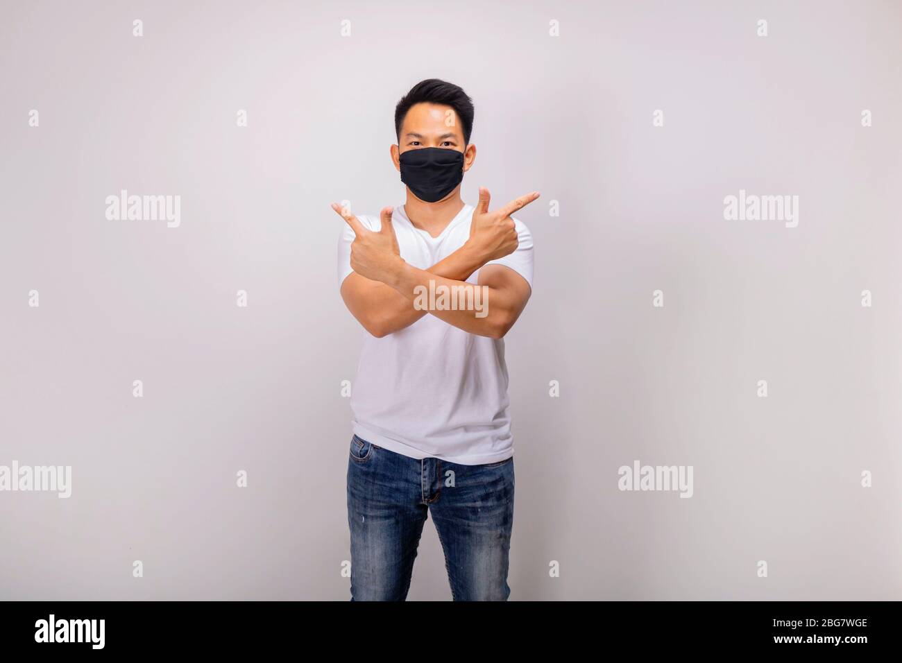 Ein asiatischer Kurzhaarmann in weißer Casual und Jeans posiert vor der Kamera in der Studiobeleuchtung, während er schwarze Maske trägt Stockfoto