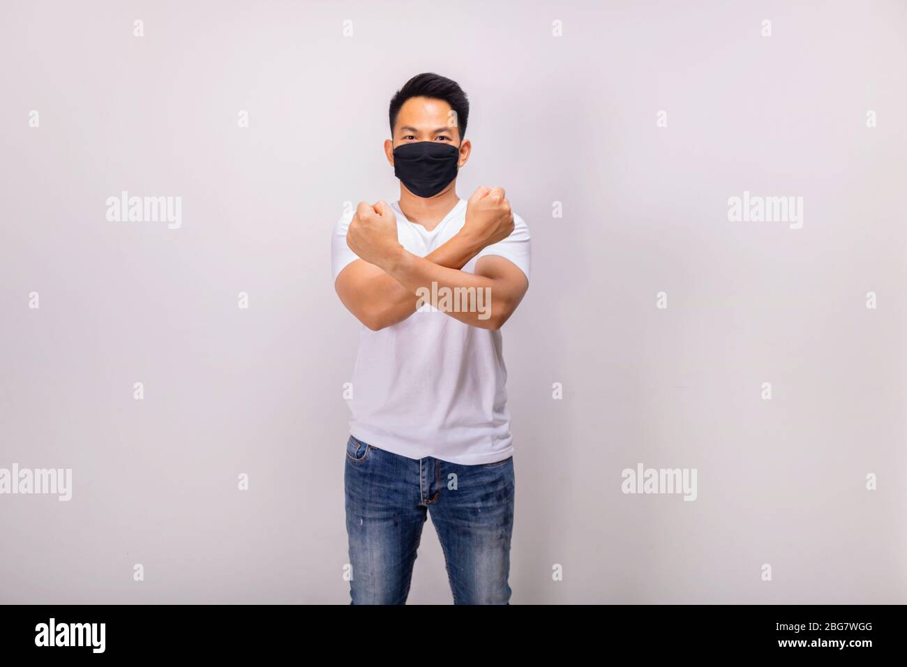 Ein asiatischer Kurzhaarmann in weißer Casual und Jeans posiert vor der Kamera in der Studiobeleuchtung, während er schwarze Maske trägt Stockfoto