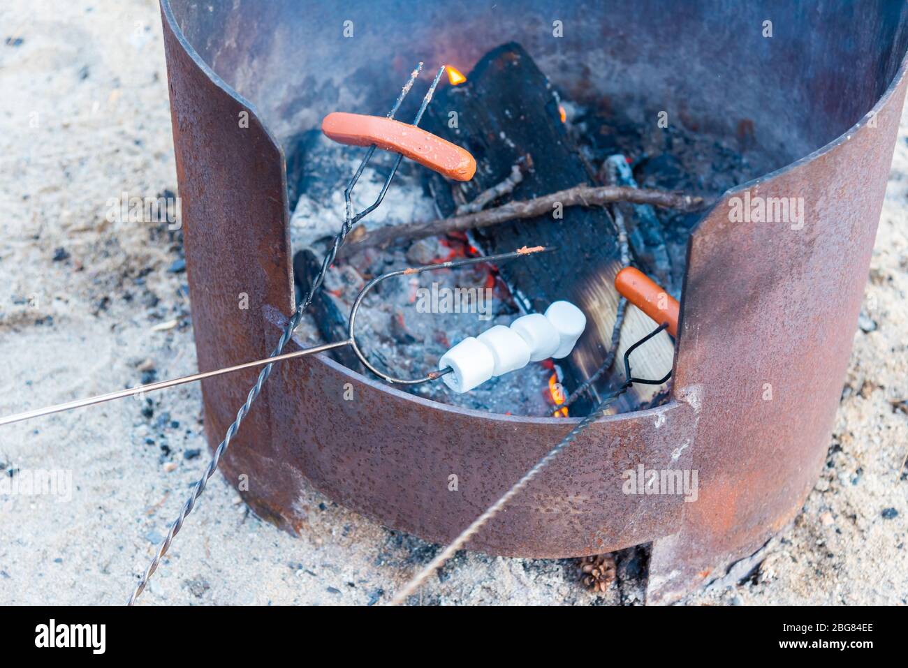 Nahaufnahme von Hot Dogs und Marshmallows, die auf Röstersticks über dem Lagerfeuer kochen Stockfoto