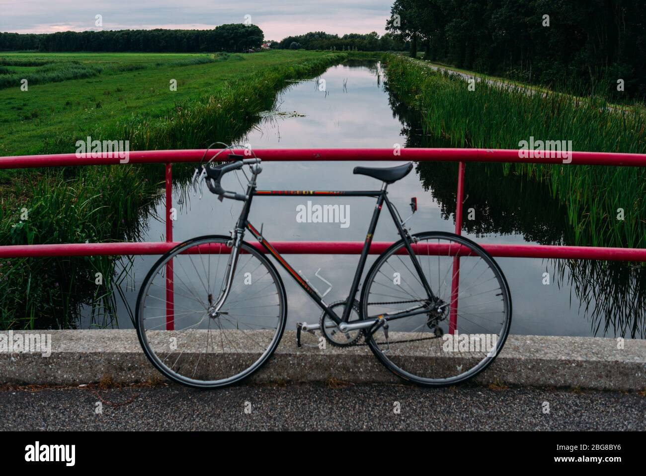 Vintage peugeot Rennrad lehnt auf einer rosa Brücke. Grün ausgekleideten Kanal, im Hintergrund Stockfoto