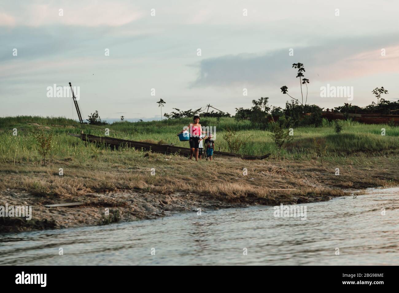 Mutter hält Wäsche steht bei ihren Söhnen am Amazonas-Ufer in der Dämmerung - Dschungelleben in der Nähe von Iquitos, Peru Stockfoto