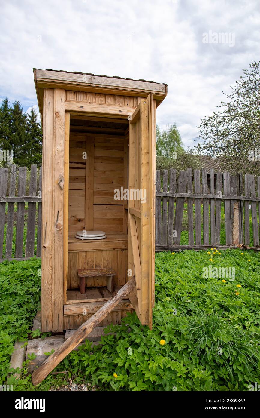 Tradition, rustikale HolzToilette, WC, mit einem modernen Toilettensitz mit Deckel, im Hof, vor dem Hintergrund eines alten Zauns. Stockfoto