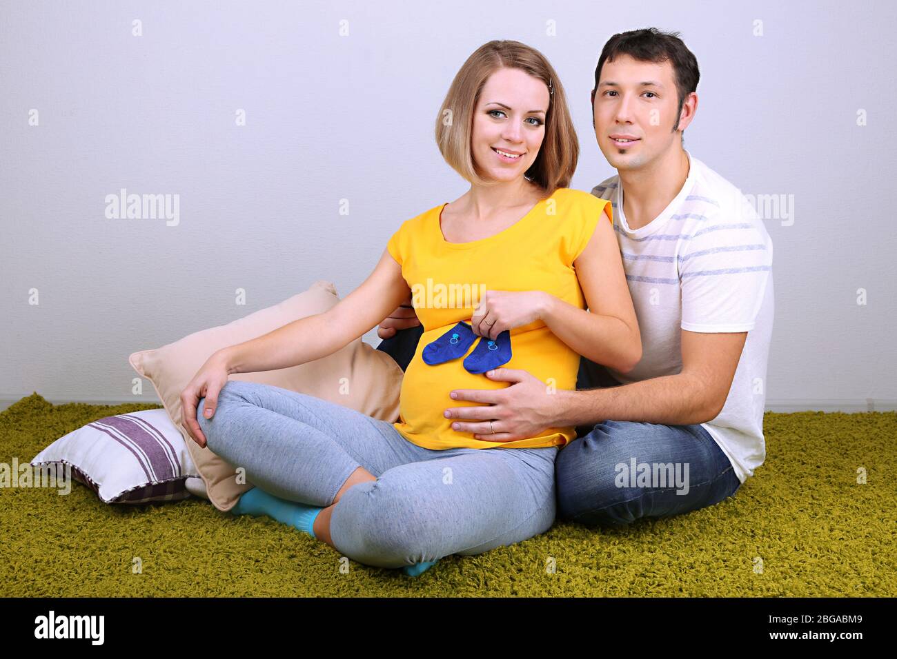 Junge schwangere Frau hält Baby Socken mit ihrem Mann auf dem Boden zu Hause Stockfoto