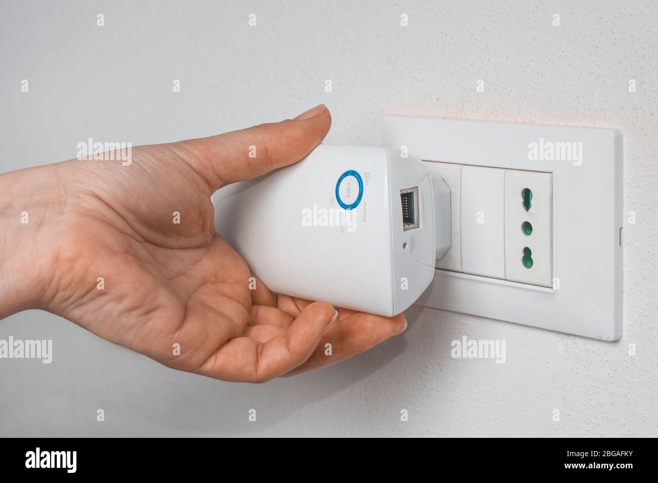 Frau einen WLAN-Repeater an einen Wandstecker anschließen Stockfoto