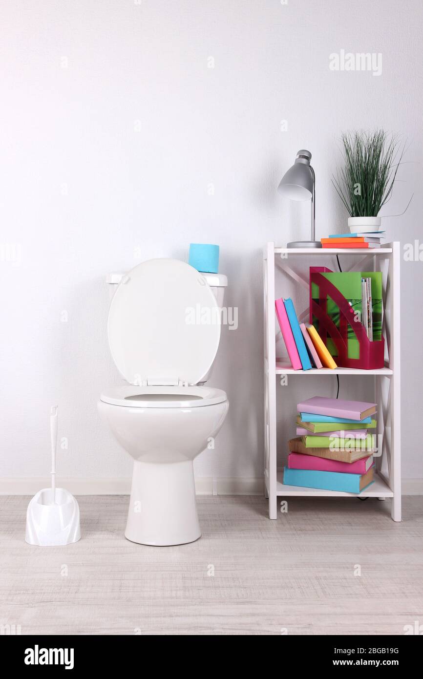 Weiße Toilettenschüssel und Ständer mit Büchern, auf farbigen Wandhintergrund Stockfoto