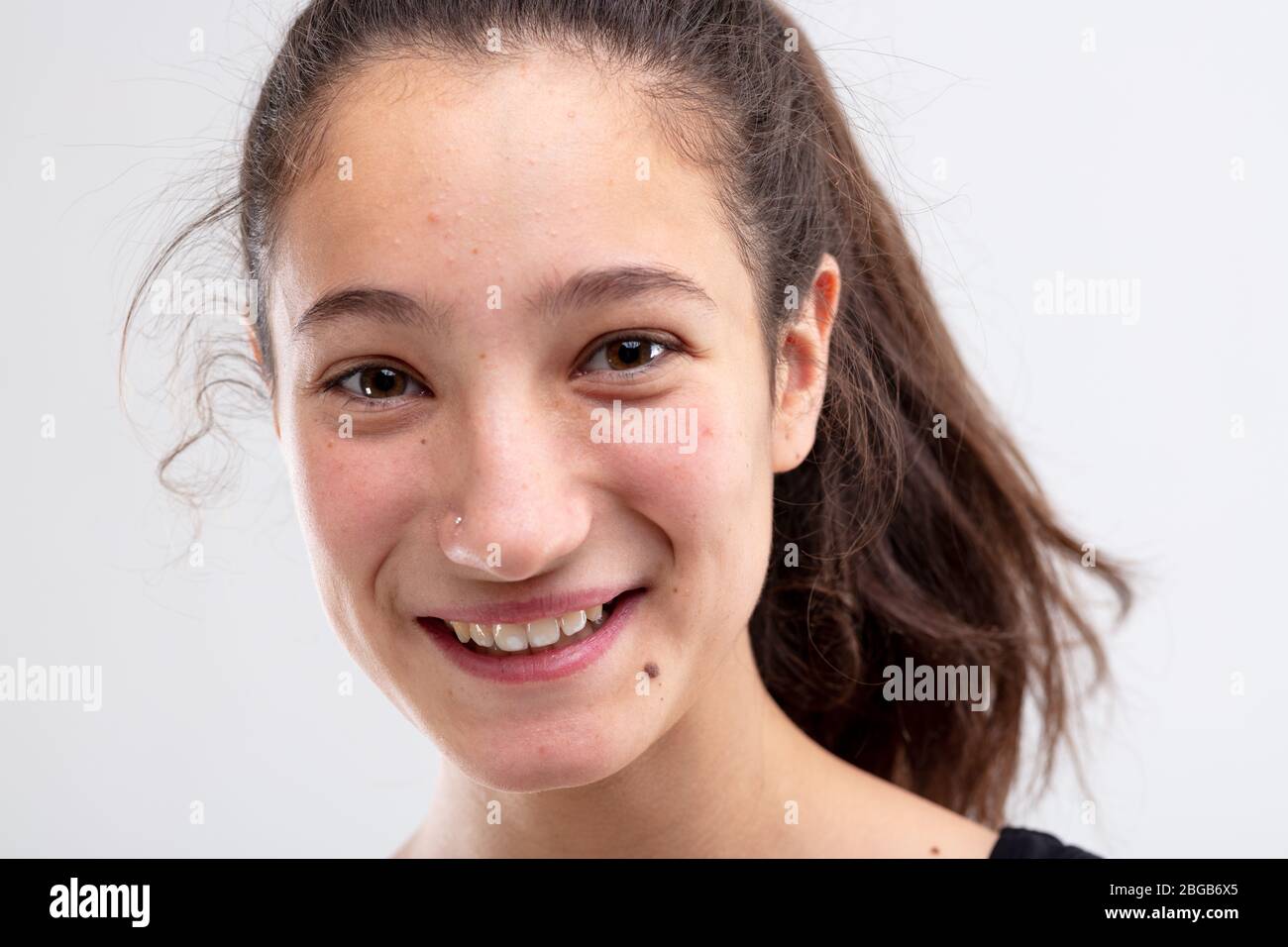 Fröhliche junge Frau grinst mit einem fröhlichen Ausdruck in einer Nahaufnahme auf weißem Kopf Stockfoto