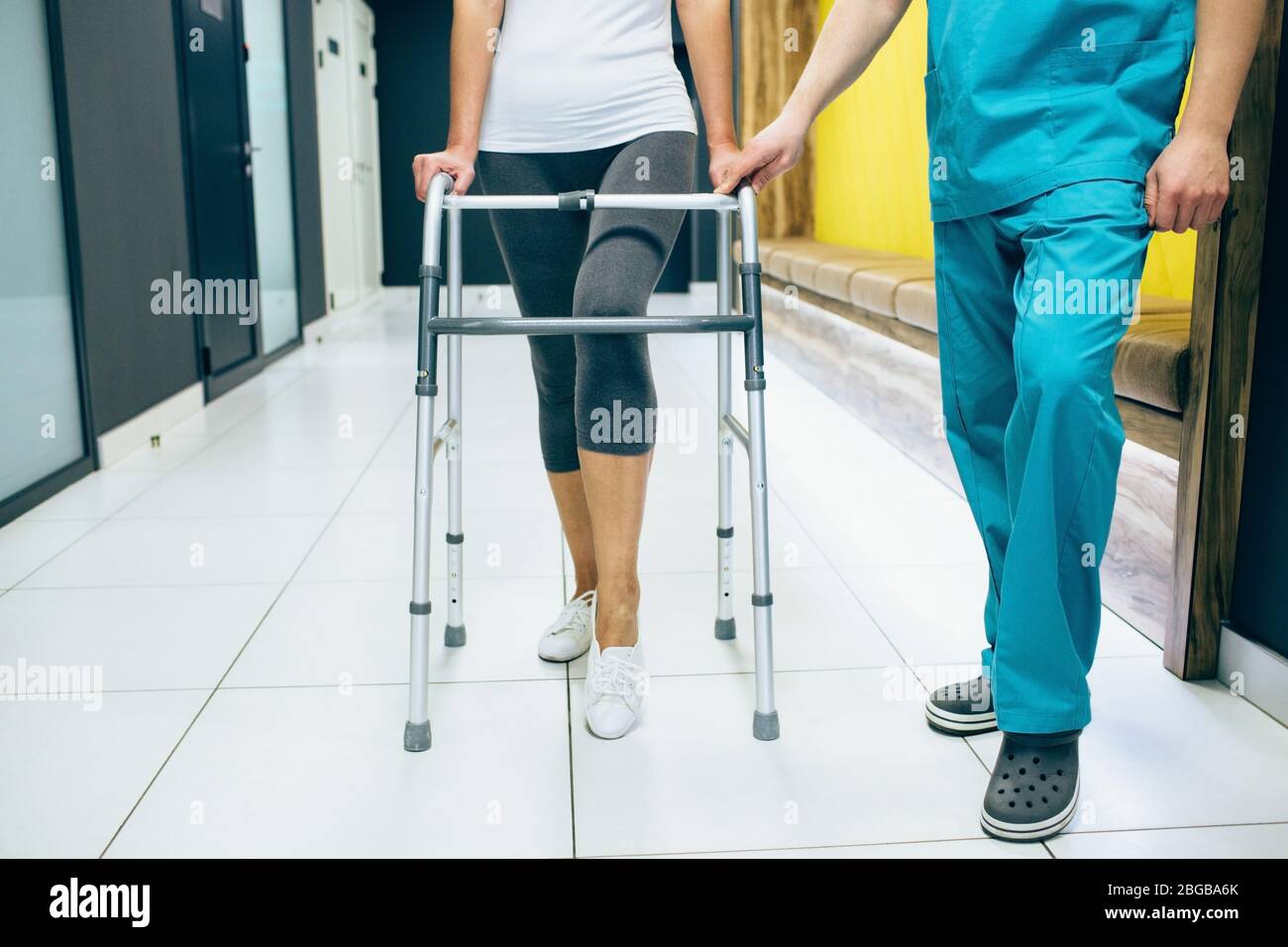 Frau mit einem Geher, geht entlang des Korridors einer modernen Rehabilitationsklinik. Rehabilitiologe hilft Patienten beim Gehen. Rehabilitation nach Verletzungen Stockfoto