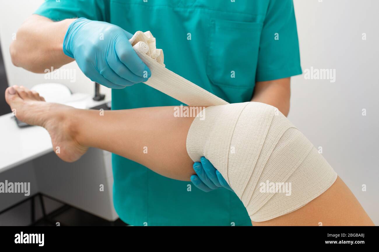 Knieverbandungsprozess des Patienten mit elastischer Bandage zur Fixierung des Kniegelenkes in fixierter Position. Physiotherapeut Bandage Knie Nahaufnahme Stockfoto