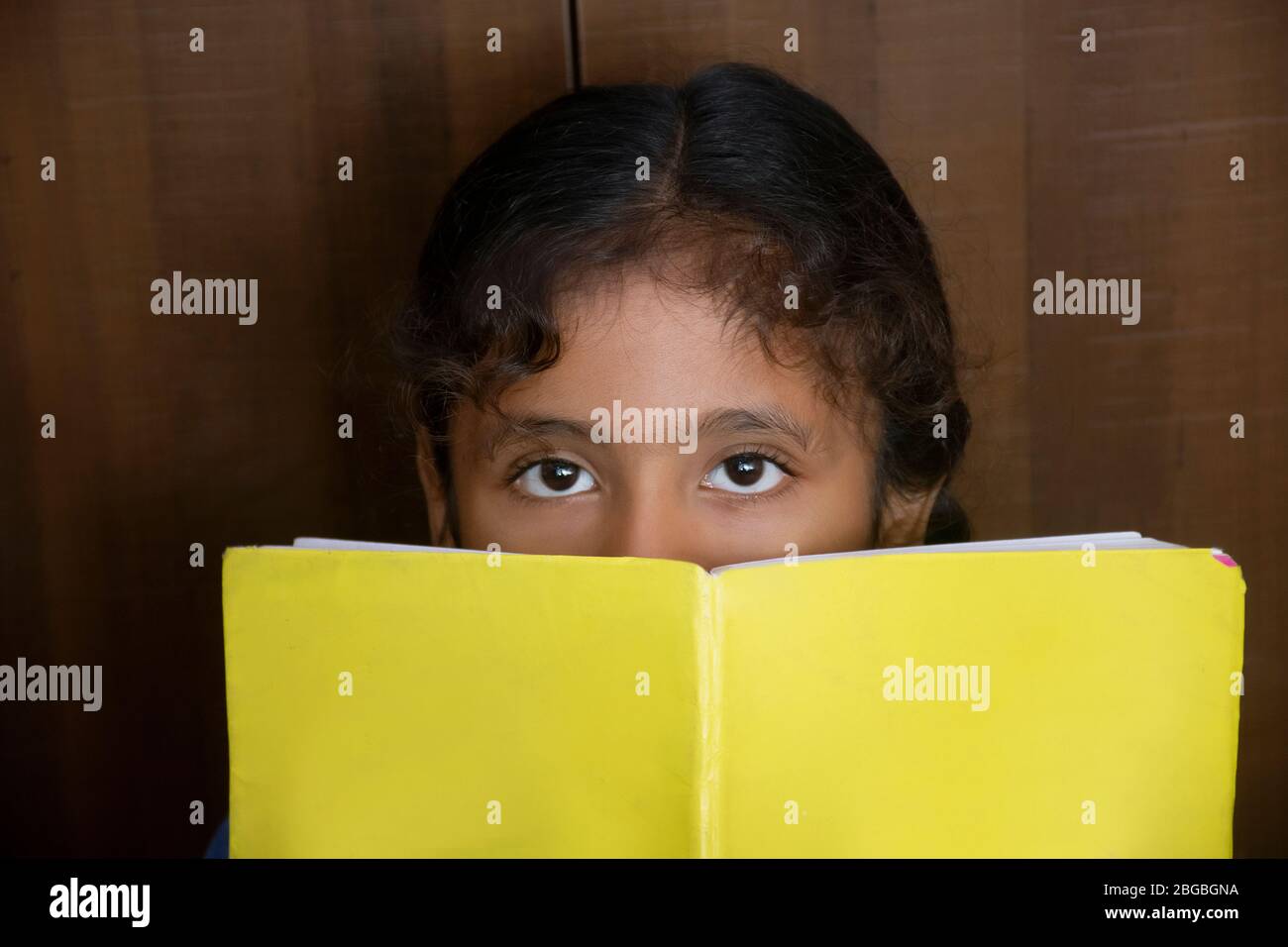 Schulmädchen bedeckte ihr Gesicht mit Buch Stockfoto