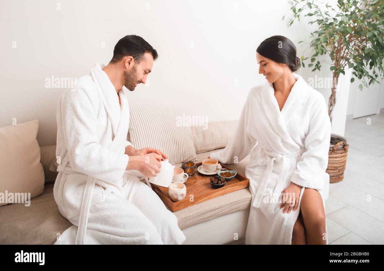 Mann gießt Wellness Tee zu schönen Frau im Spa nach der Massage. Pärchen, die sich im Resort und Spa-Salon ausruhen Stockfoto
