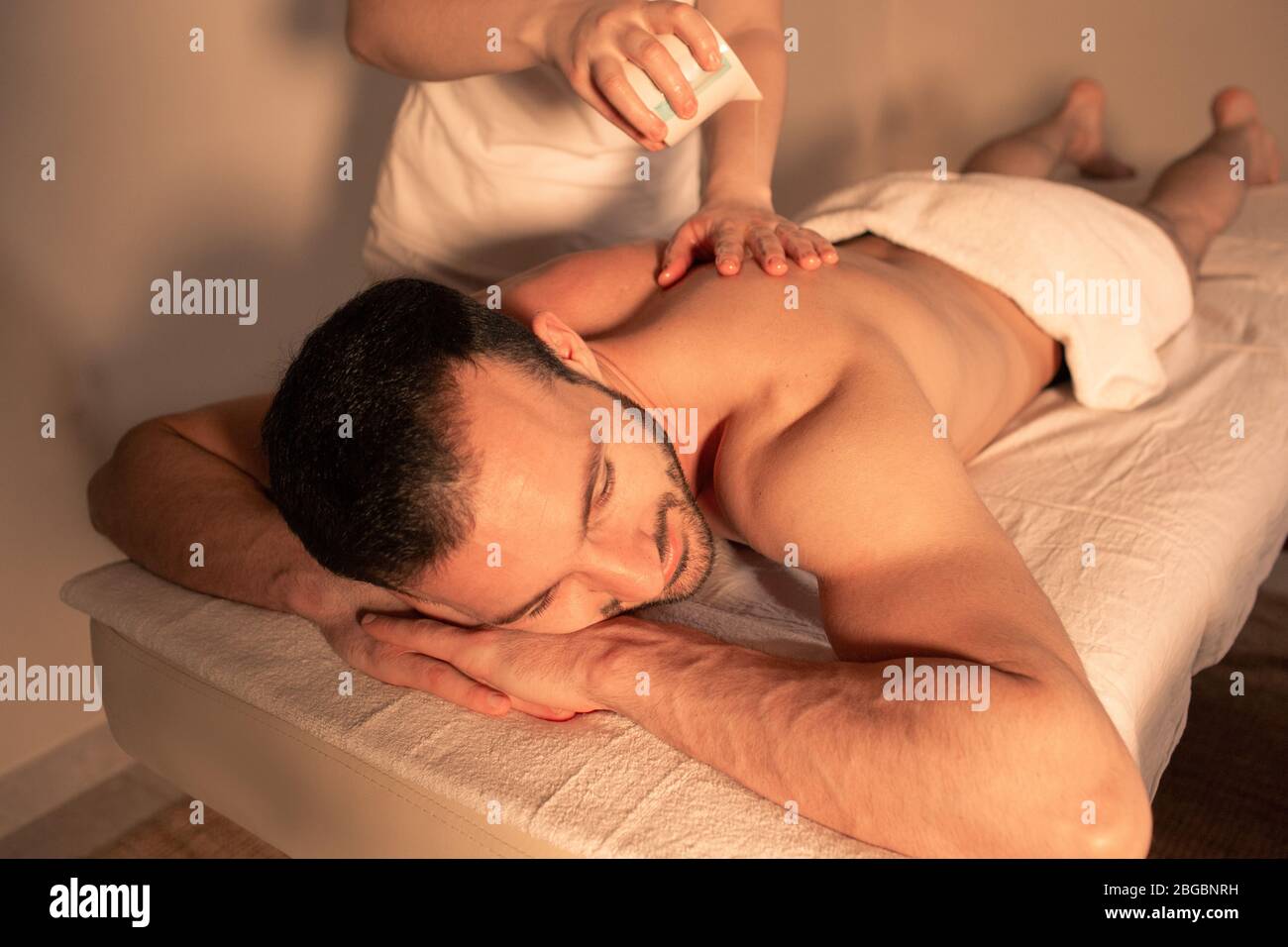 Mann genießt entspannende Massage mit Aromaöl und brennender Kerze. Gemischter Renner verbringt Zeit im Spa und bekommt Aromatherapie, heiße Ölmassage. Stockfoto