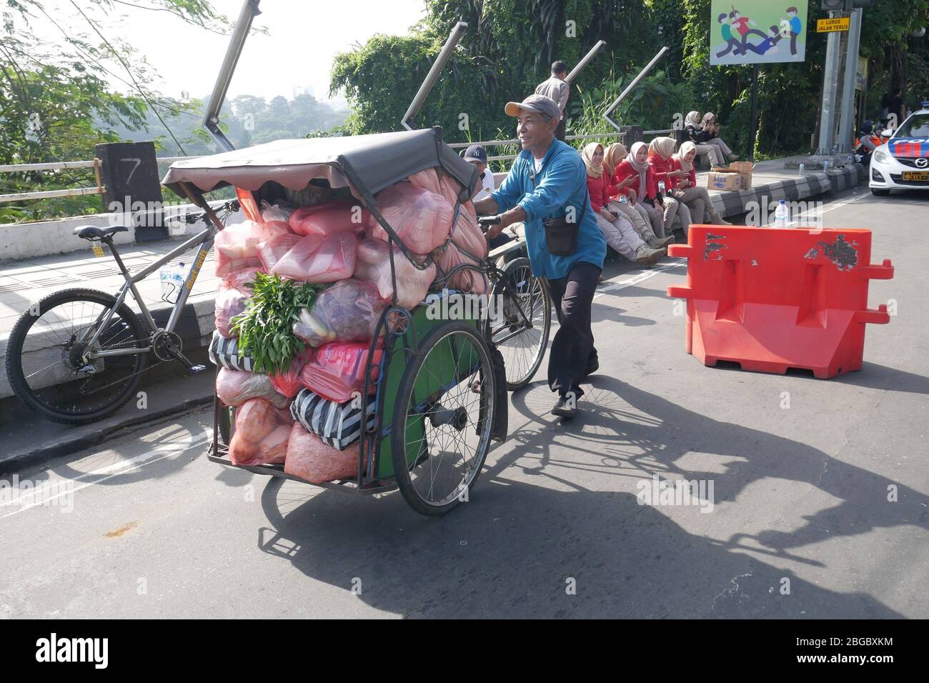Ein Mann schiebt eine Rikscha voller Gemüse und Waren in Plastiktüten. Stockfoto