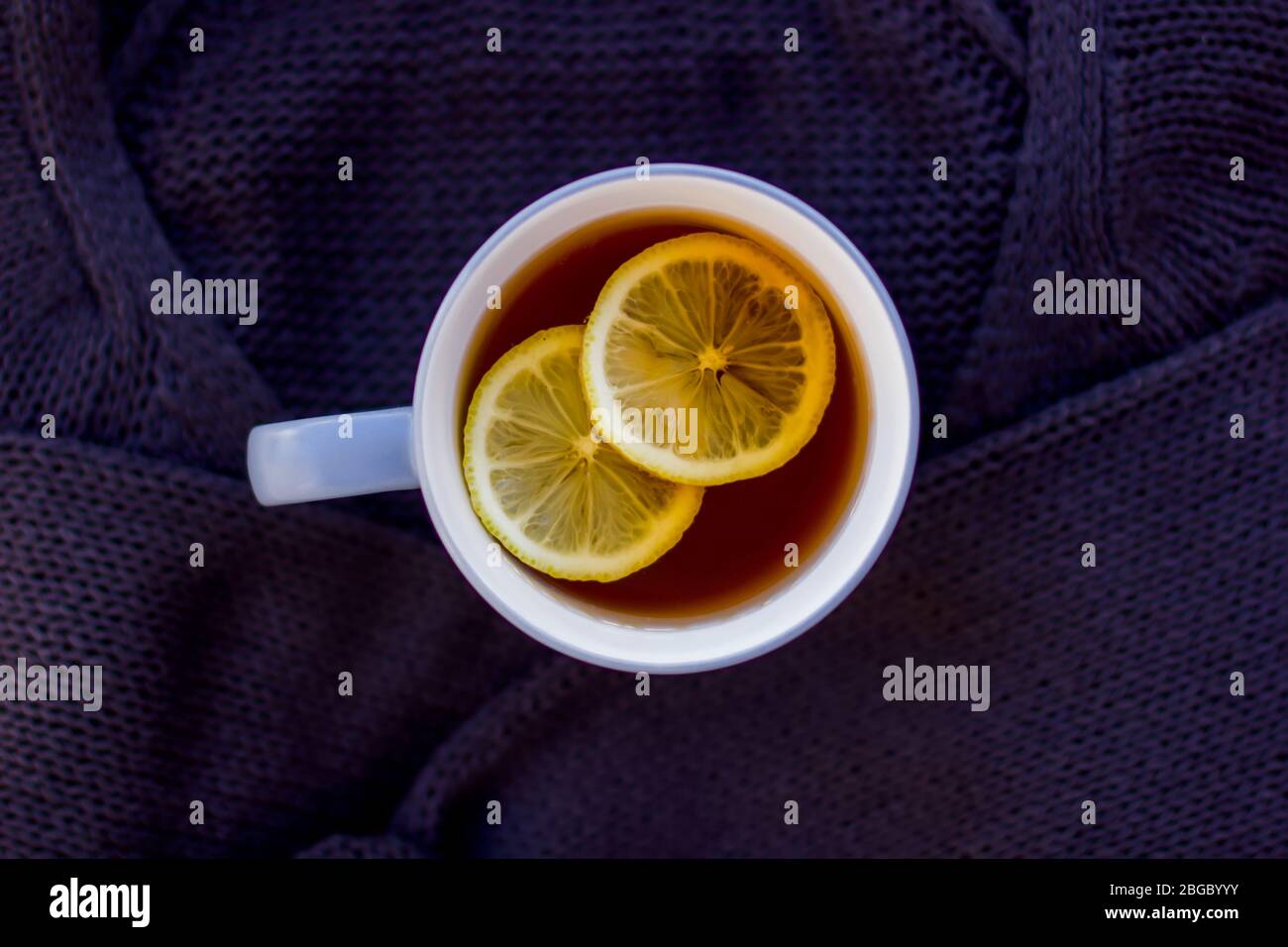 Herbstgestaltung mit heißem Tee mit Zitrone auf einem Pullover und trockenen Blättern. Brauner Hintergrund. Stockfoto