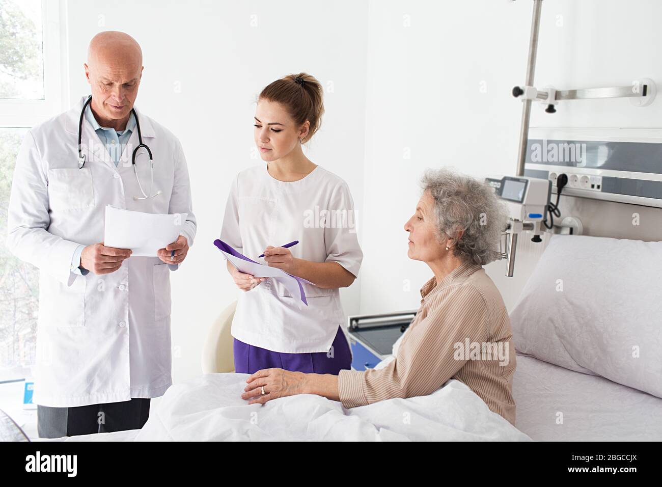 Teamarbeit, Arzt und Krankenschwester stehen auf der Station in der Nähe von älteren Patienten, sie sehen ein Bild von einem Röntgenbild der Wirbelsäule. Krankenhausstation Stockfoto