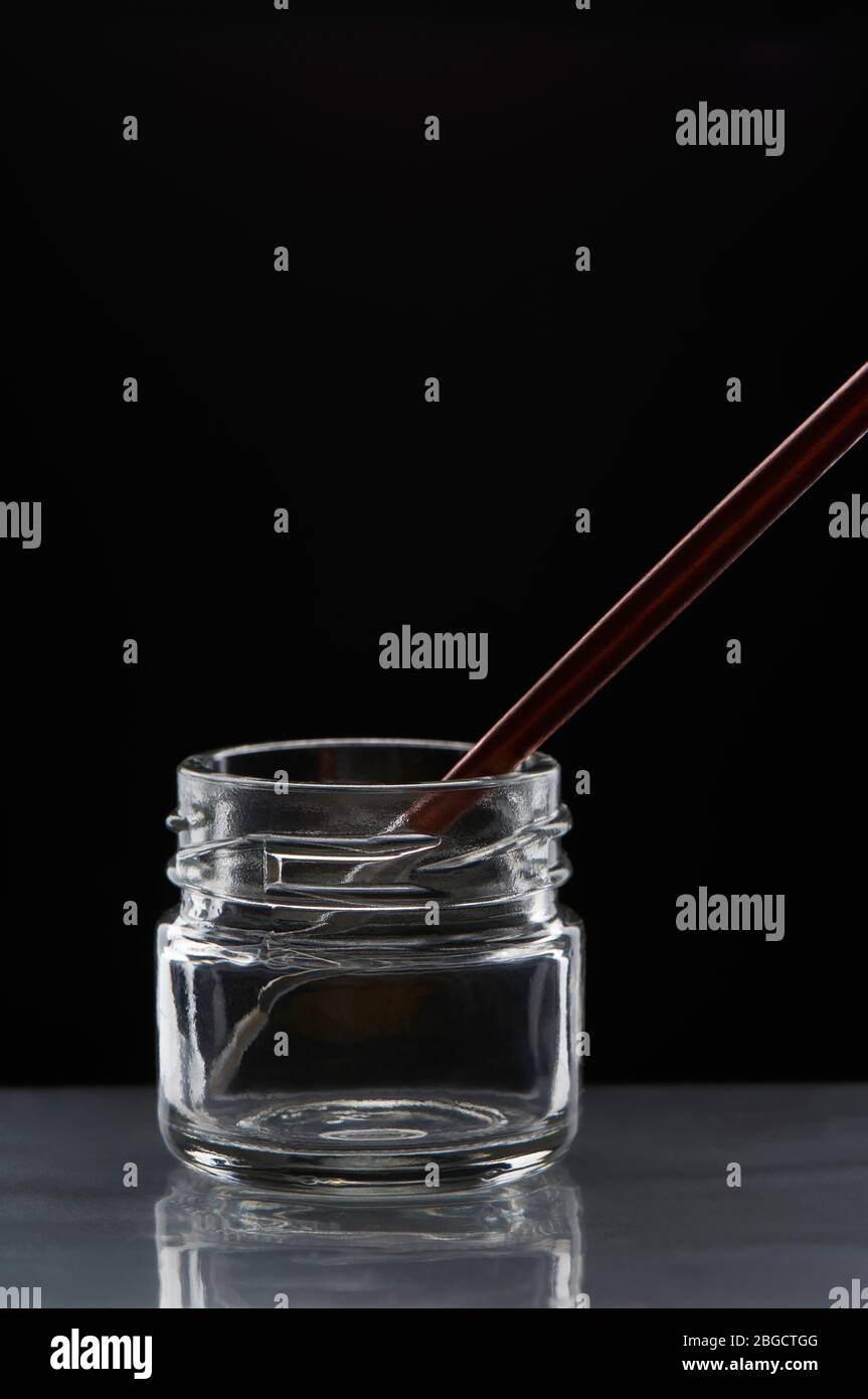 Pinsel mit dem kastanienbraunen Griff in einem leeren transparenten Glas auf schwarzem Hintergrund. Stockfoto