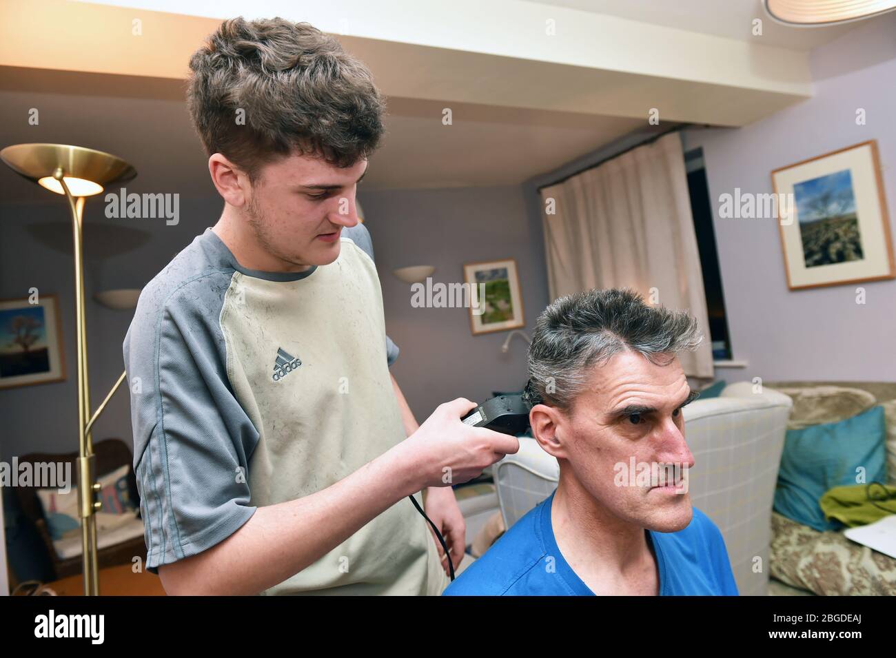 Leben bei der Sperrung des Coronavirus in Großbritannien April 2020. Sohn, der seinem Vater die Haare mit Haarschneidern schneidet. Modell freigegeben. Stockfoto