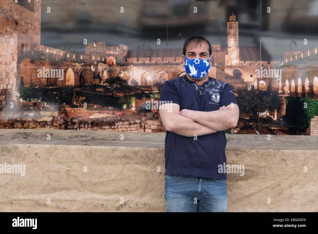 Ein israelischer Mann, der eine Gesichtsmaske trägt, die mit dem jüdischen Davidstern wegen der COVID-19-Pandemie des Coronavirus geschmückt ist, steht vor einem Plakat, das den befestigten Turm Davids darstellt, auch als Jerusalemer Zitadelle in Westjerusalem Israel bekannt Stockfoto