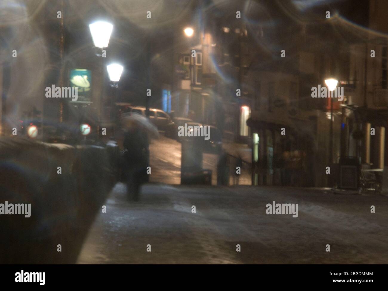 Ein stimmungsvolles Bild von Menschen, die nachts in einer Fußgängerzone in starkem Regen gefangen sind, und Straßenlaternen, die ein unheimliches Leuchten bringen Stockfoto