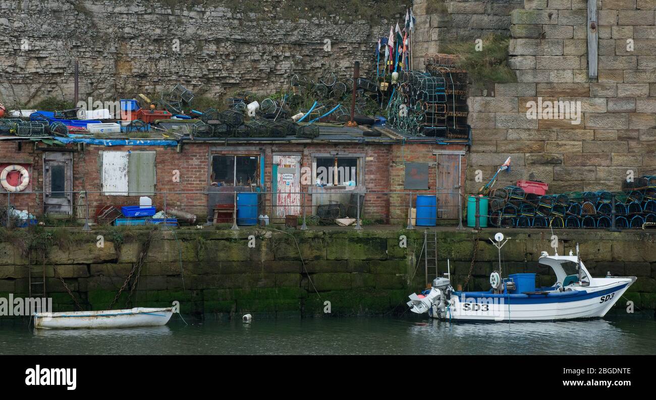 Der alte Hafen von Seaham zeigt kleine Gebäude im Inneren des Hafens, zusammen mit Hummer-Töpfen, Markierungsfahnen und einem kleinen Fischerboot Stockfoto