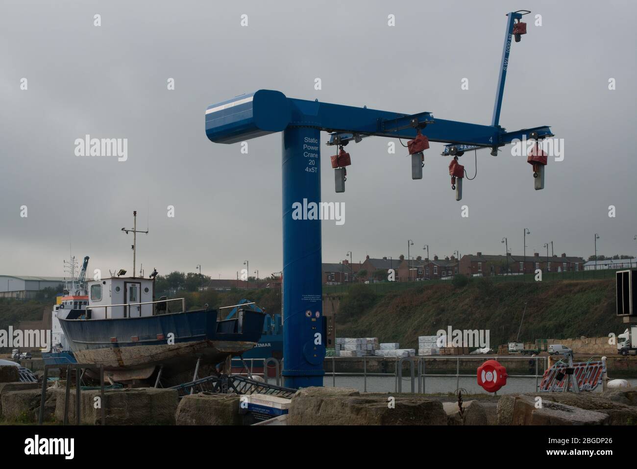 Statischer Stromkran am Seaham Hafen mit erhöhtem Kleinboot am Hafen und Reihenhaus der Stadt im Hintergrund Stockfoto