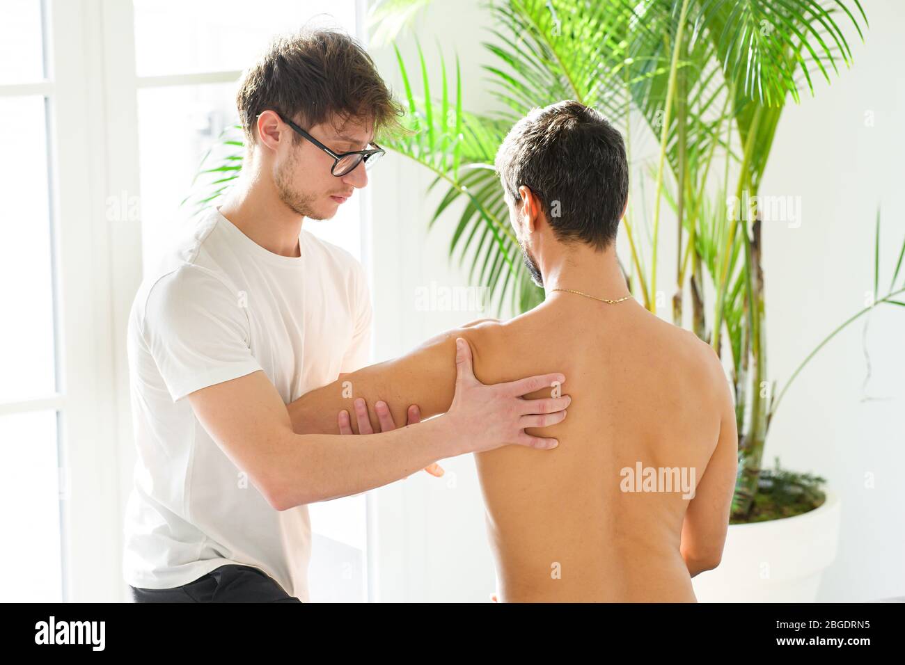 Osteopath Beurteilung der Schulterblatt, Schulterblatt, Flügelbein oder Klingenknochen eines jungen Mannes in seiner Klinik in einer Nahaufnahme High Key View Stockfoto